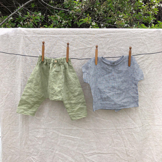 Green shorts and blue striped shirt hanging on a clothesline with a natural background.