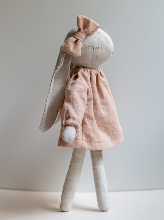 Stuffed bunny toy wearing a pink dress on a plain background