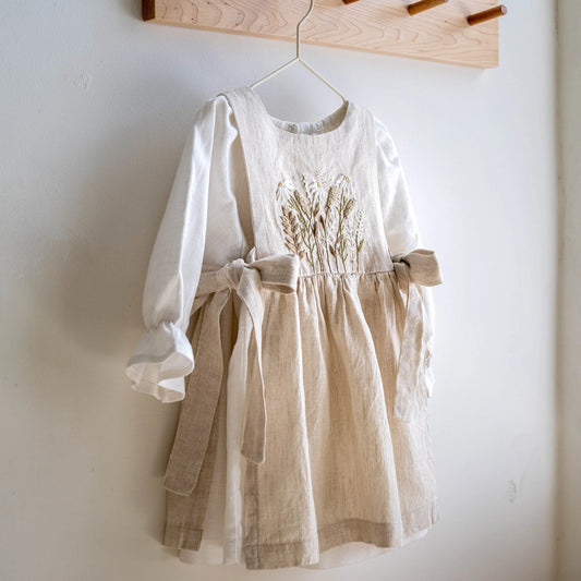 White dress with beige skirt on a hanger against a white wall