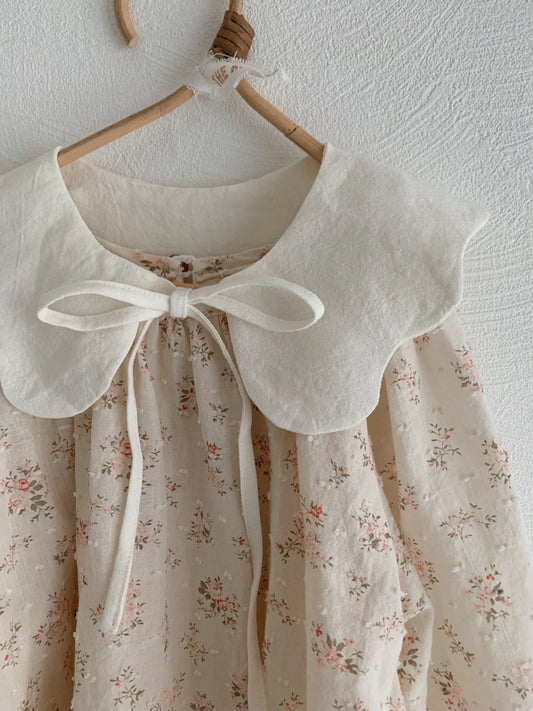 Floral dress with a large bow on a hanger against a white wall