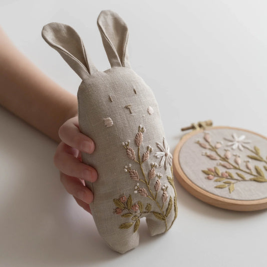 Hand holding a embroidered rabbit toy with a matching hoop on a light background