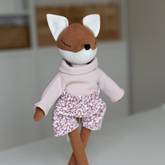 Stuffed toy fox wearing a pink sweater and floral shorts on a plain background