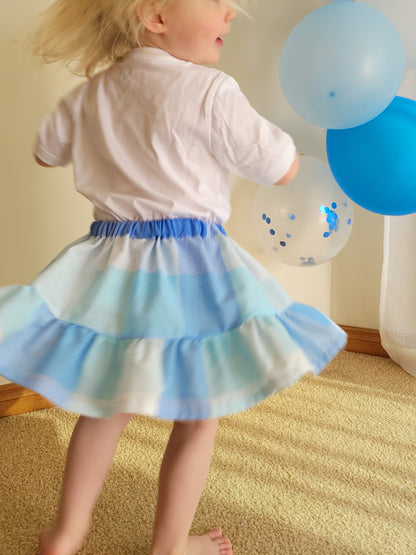 Child wearing a blue and white striped skirt with balloons in the background