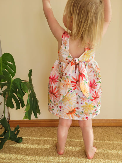 Easy beginner children’s sewing pattern for a classic dress with wide shoulder straps, empire waist, gathered skirt, and open back with bow tie detail.