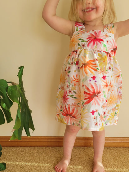 Easy beginner children’s sewing pattern for a classic dress with wide shoulder straps, empire waist, gathered skirt, and open back with bow tie detail.