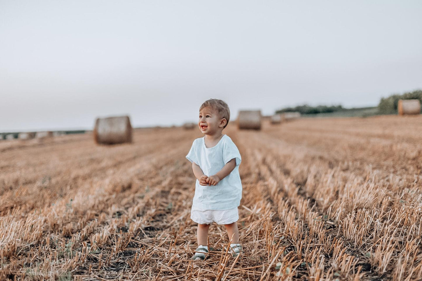 Child standing in a field with hay bales in the background