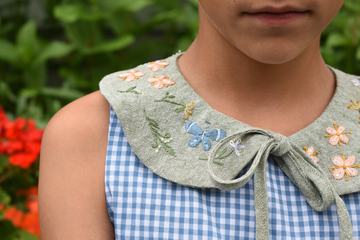 Person wearing a blue checkered dress with an embroidered green collar and flowers.