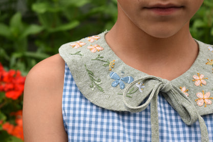 Person wearing a blue checkered dress with an embroidered green collar and flowers.