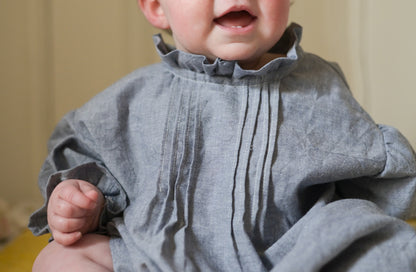 Baby wearing a gray dress with ruffled collar and sleeves.