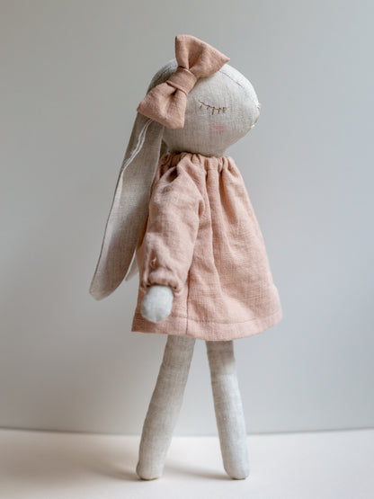 Stuffed bunny toy wearing a pink dress on a plain background