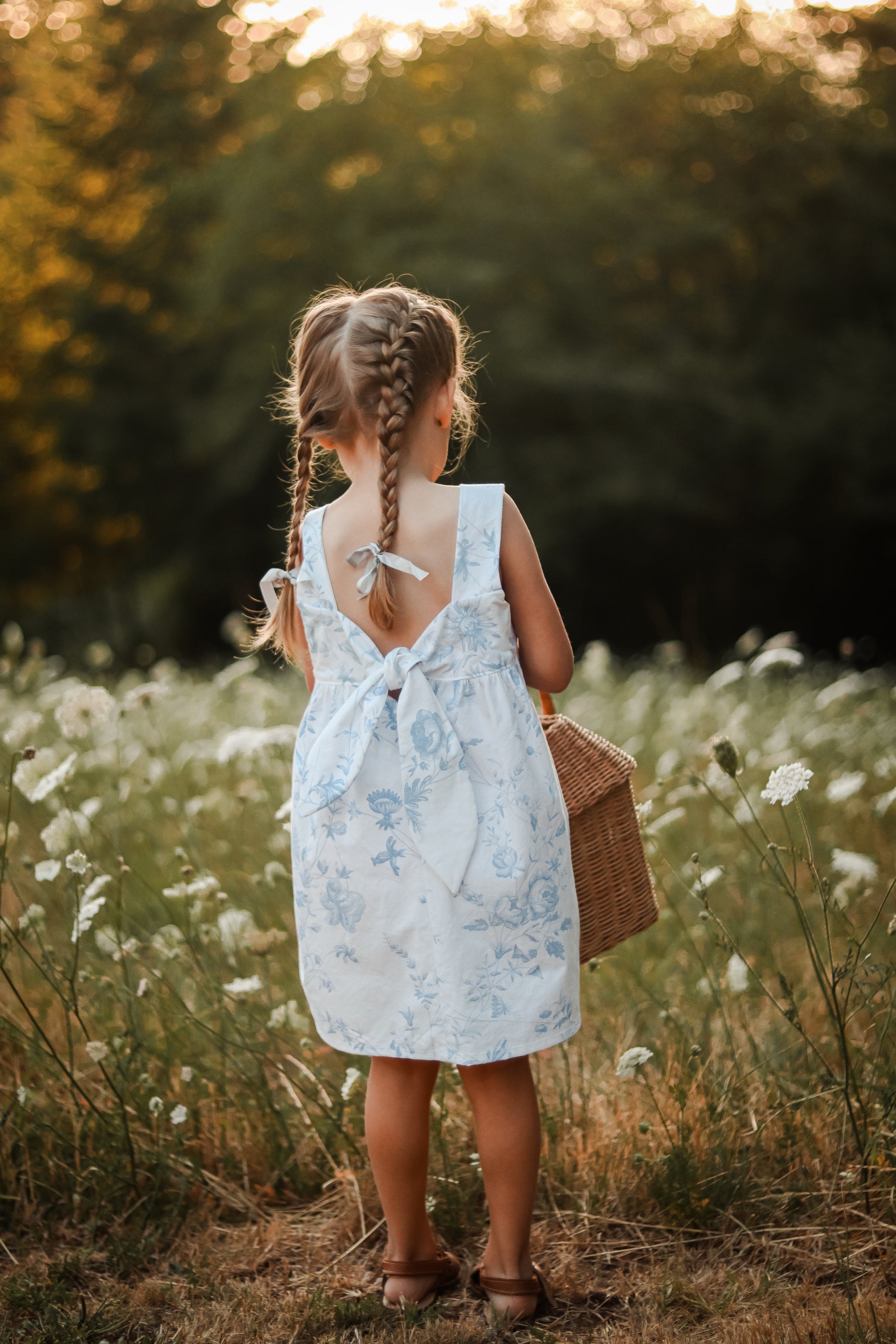 Easy beginner children’s sewing pattern for a classic dress with wide shoulder straps, empire waist, gathered skirt, and open back with bow tie detail.