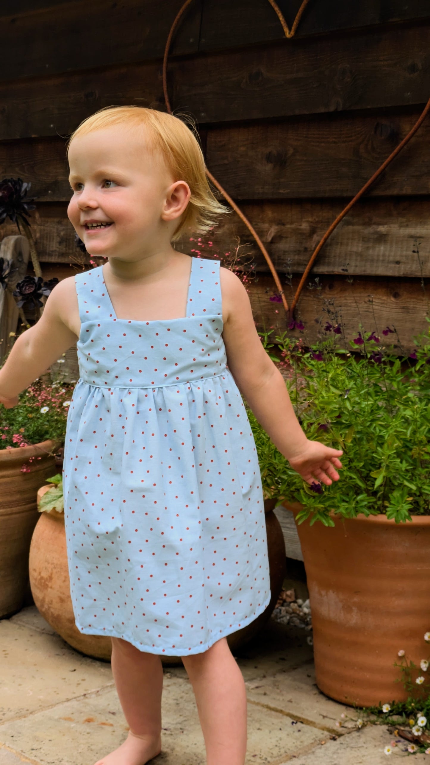 Easy beginner children’s sewing pattern for a classic dress with wide shoulder straps, empire waist, gathered skirt, and open back with bow tie detail.