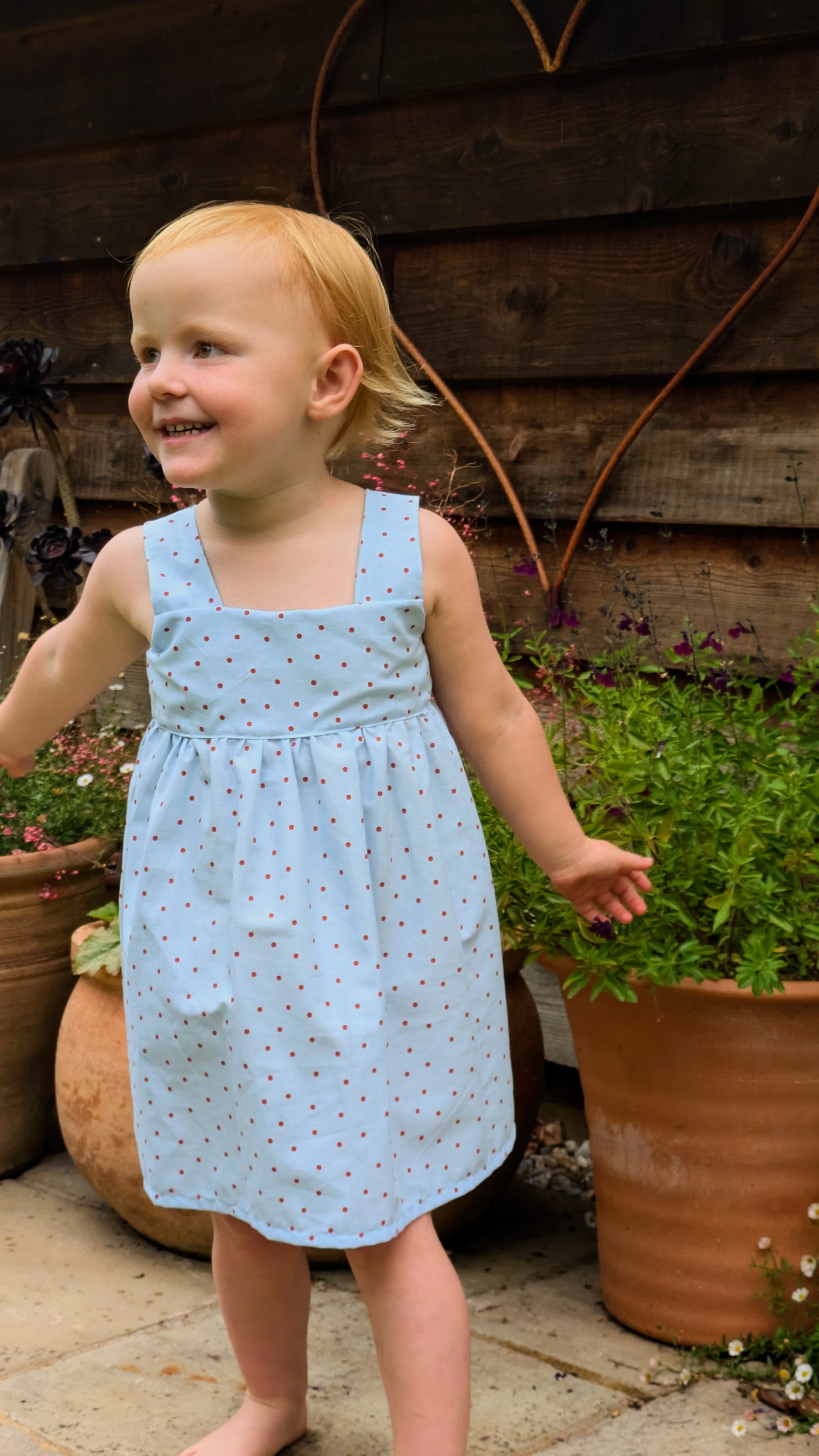 Easy beginner children’s sewing pattern for a classic dress with wide shoulder straps, empire waist, gathered skirt, and open back with bow tie detail.