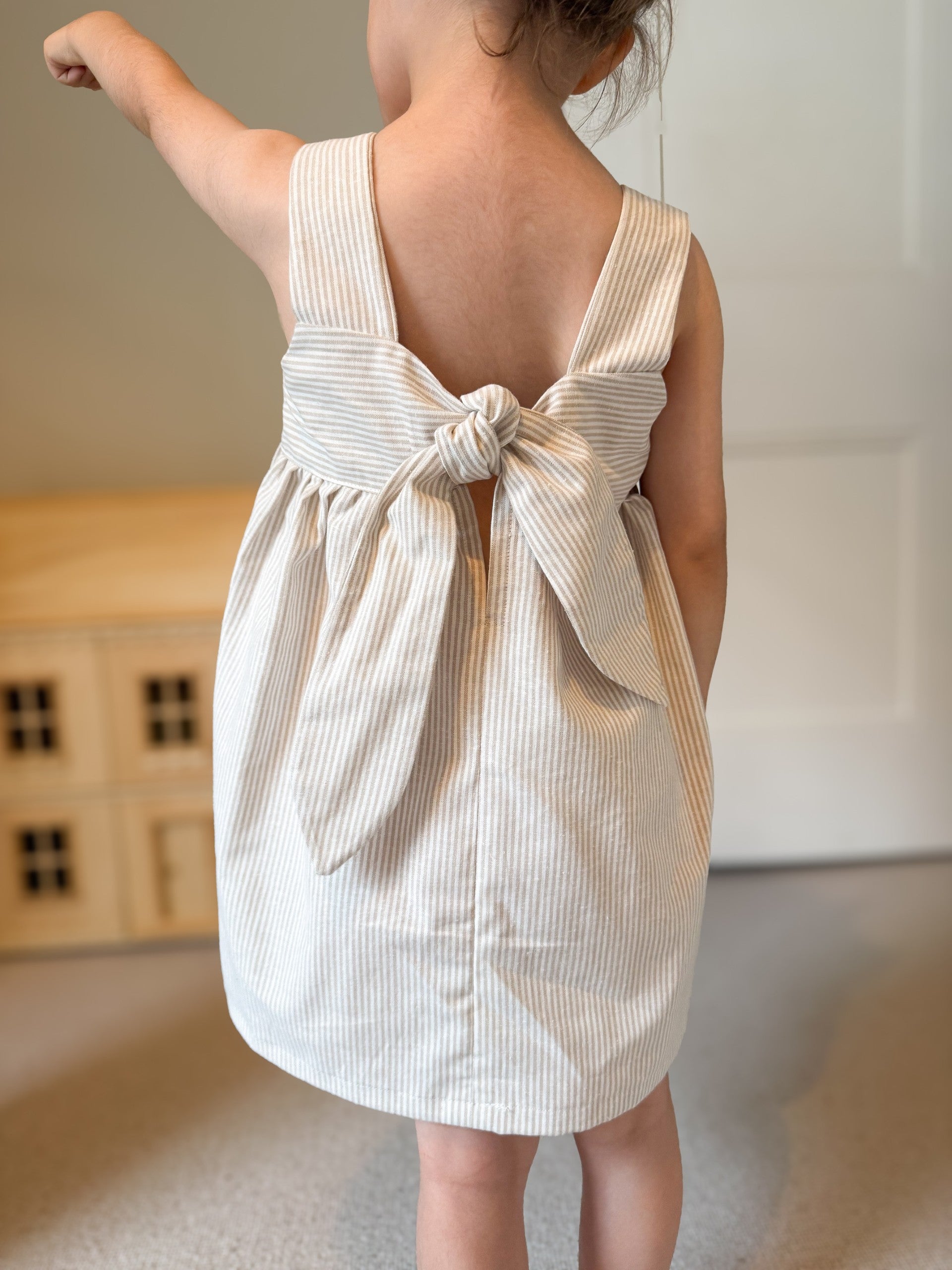 Easy beginner children’s sewing pattern for a classic dress with wide shoulder straps, empire waist, gathered skirt, and open back with bow tie detail.
