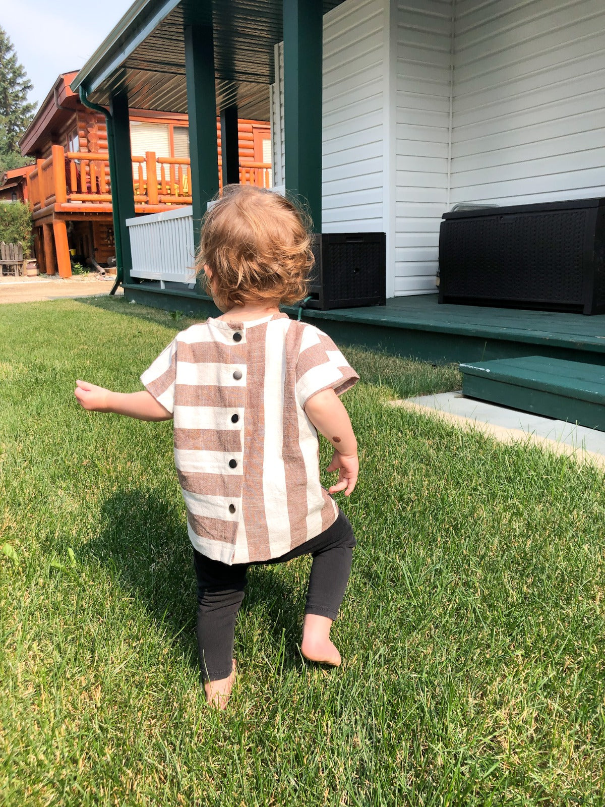 Child in a striped shirt standing on grass in front of a house