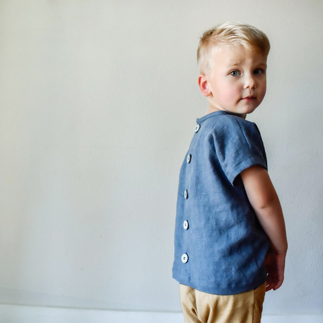 Young boy wearing a blue shirt with buttons against a plain background
