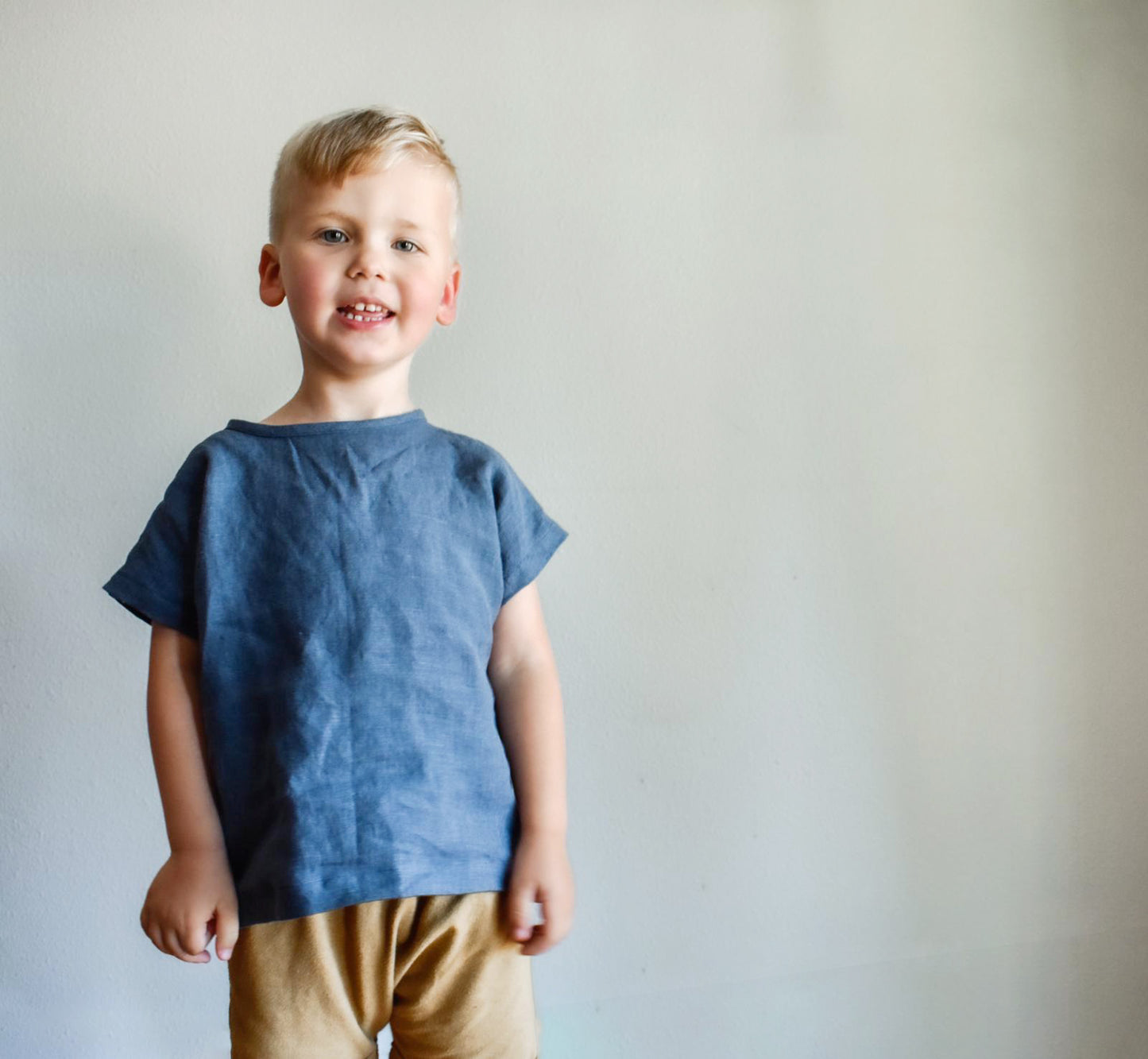 Young boy wearing a blue shirt and beige pants against a plain background