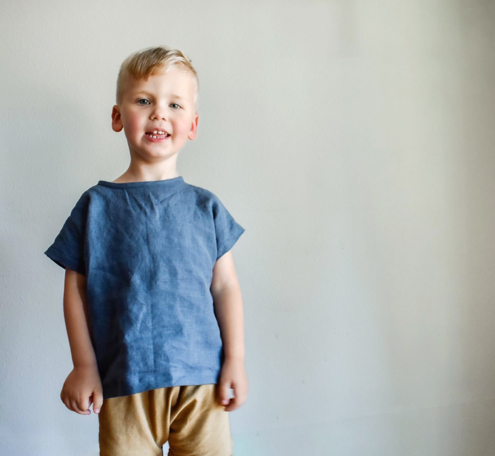 Young boy wearing a blue shirt and beige pants against a plain background