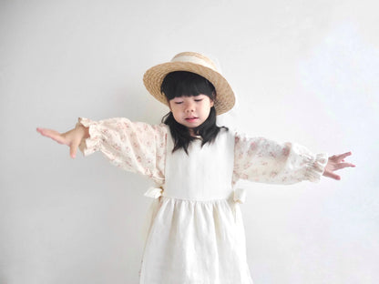 Child wearing a white dress and straw hat with arms outstretched on a plain background