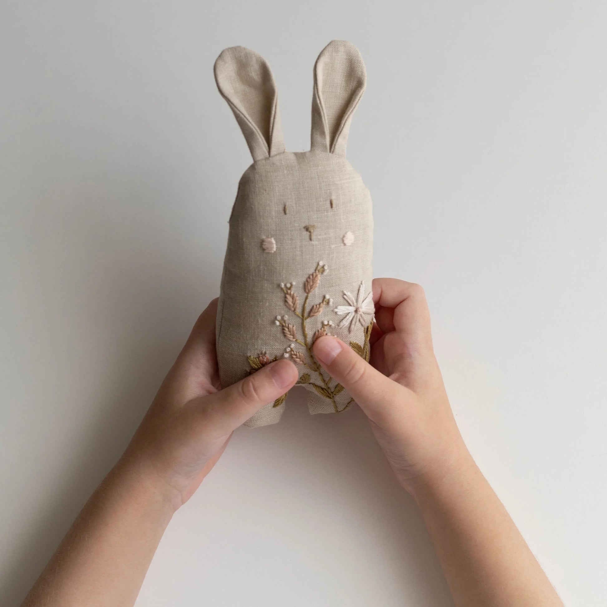 Handmade fabric rabbit with floral embroidery held by a person against a plain background