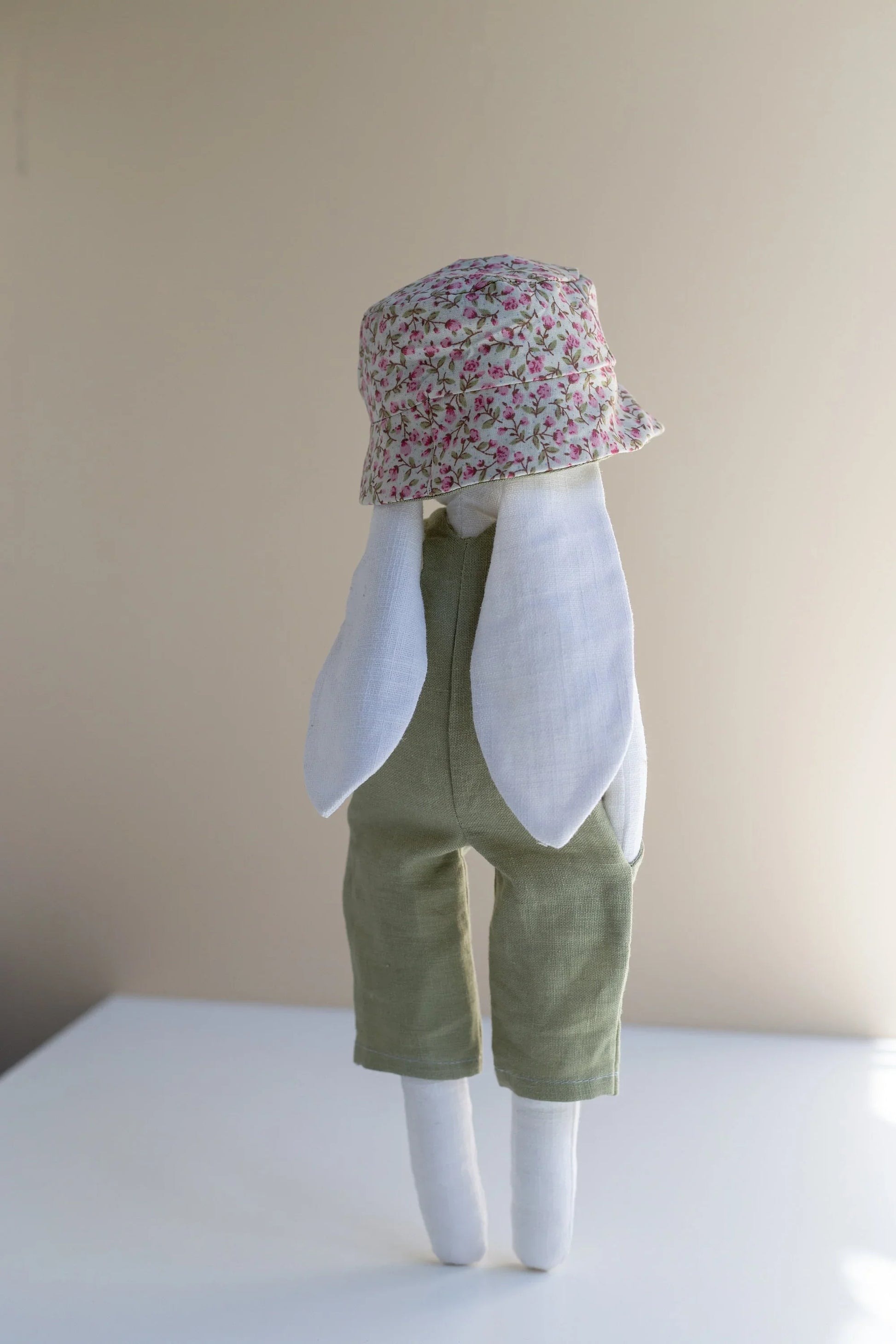 Stuffed animal wearing a floral hat and green outfit on a plain background