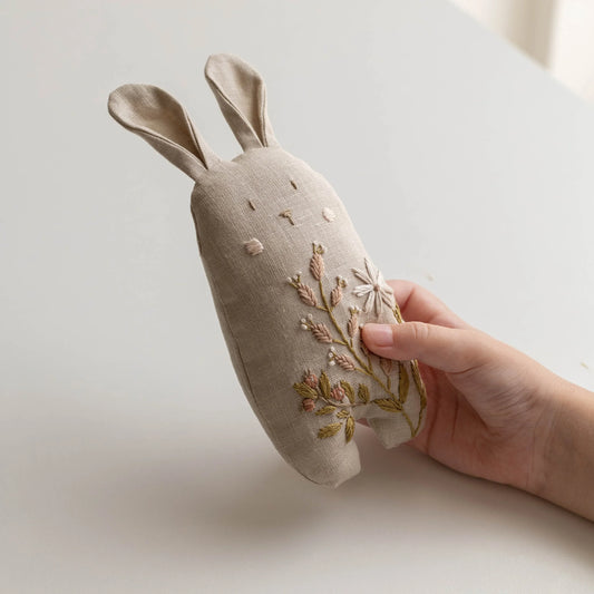 Hand holding a beige fabric rabbit with floral embroidery on a light background