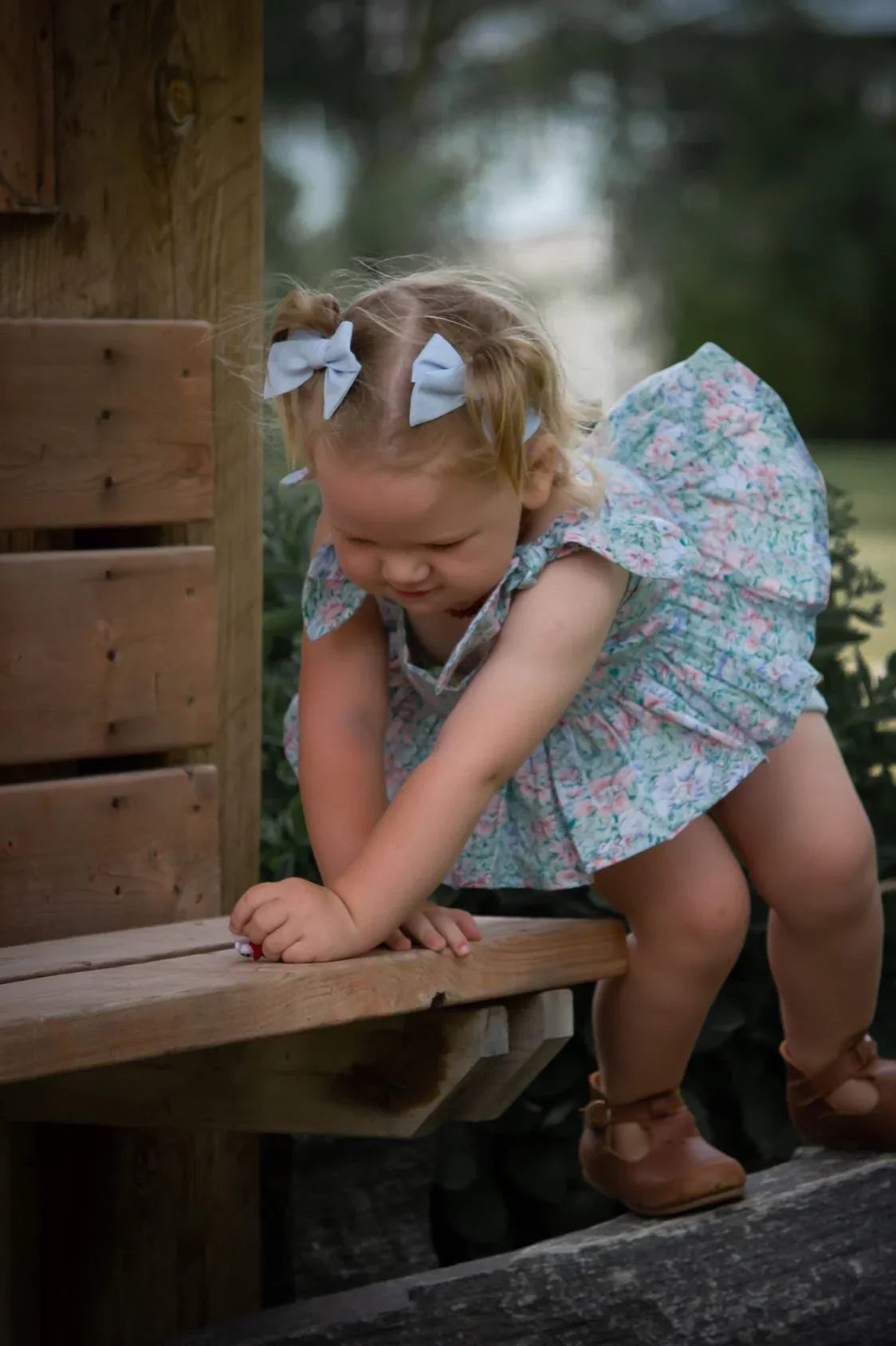 Young girl in a floral dress sitting on a wooden bench outdoors.