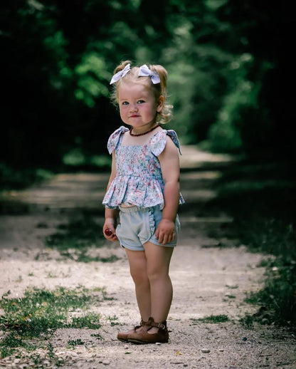 Young girl standing on a dirt path with greenery in the background