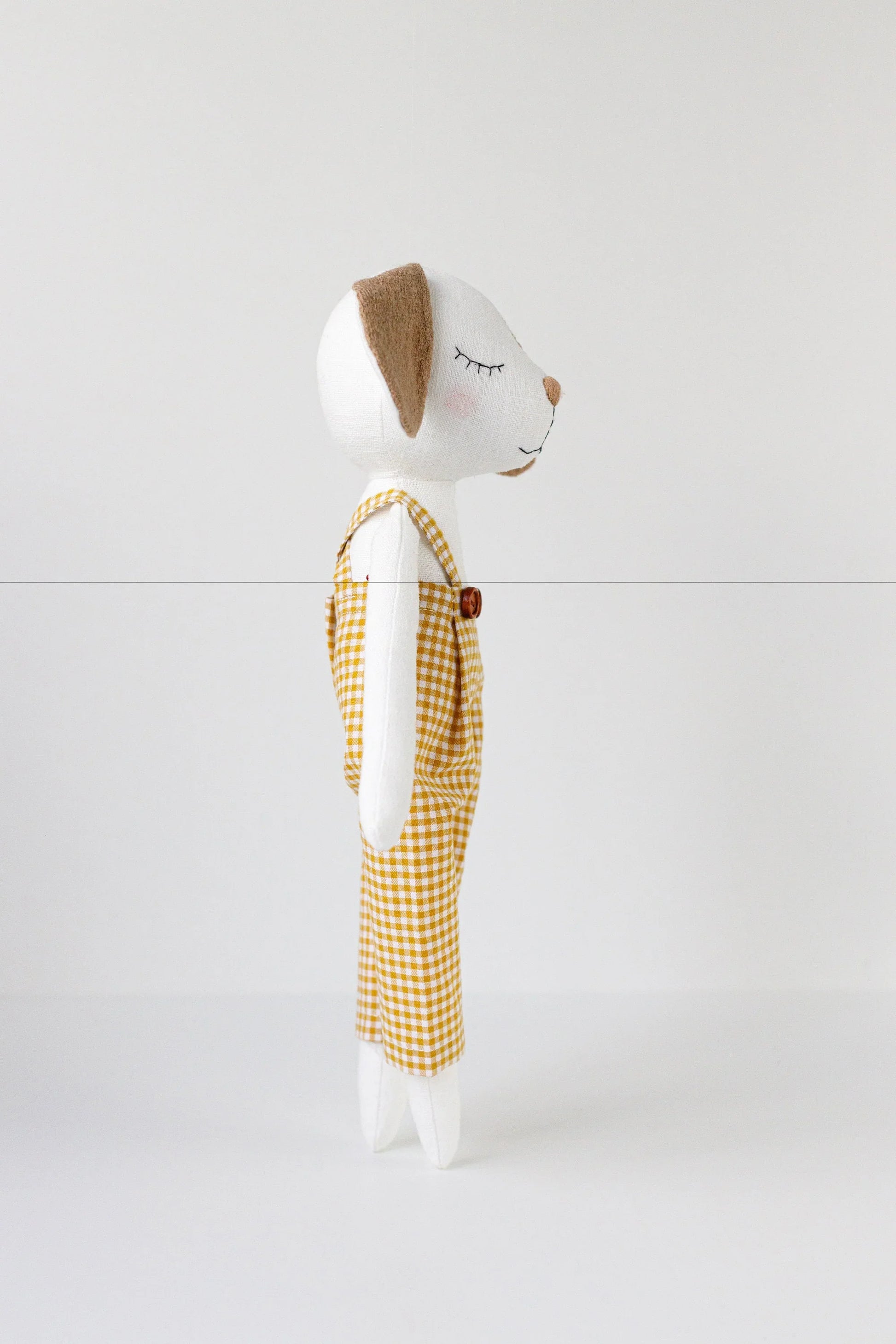 Stuffed animal toy with a white face and brown ears, wearing yellow checkered overalls on a white background.