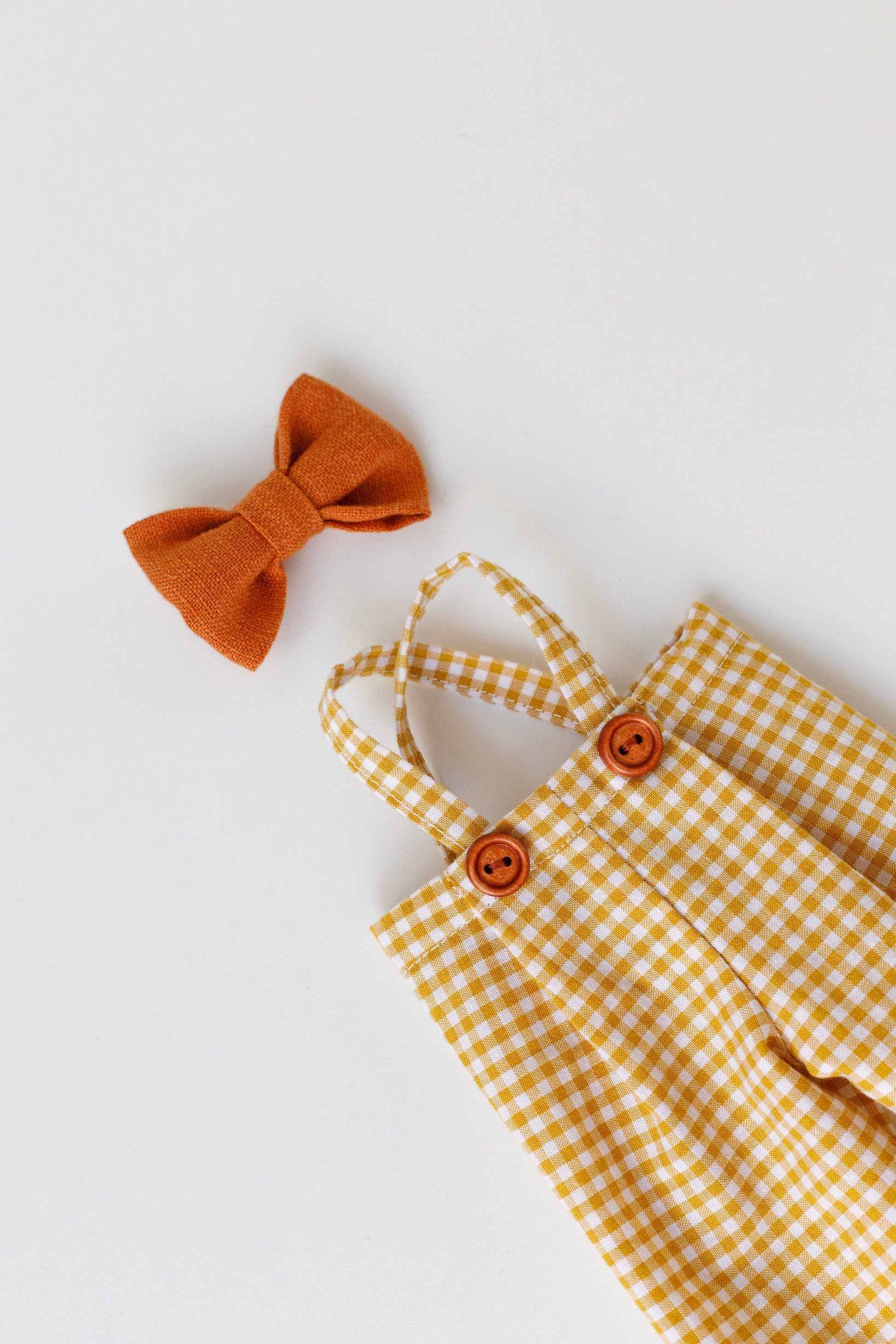 Yellow checkered dress with orange buttons and a matching bow on a light gray background