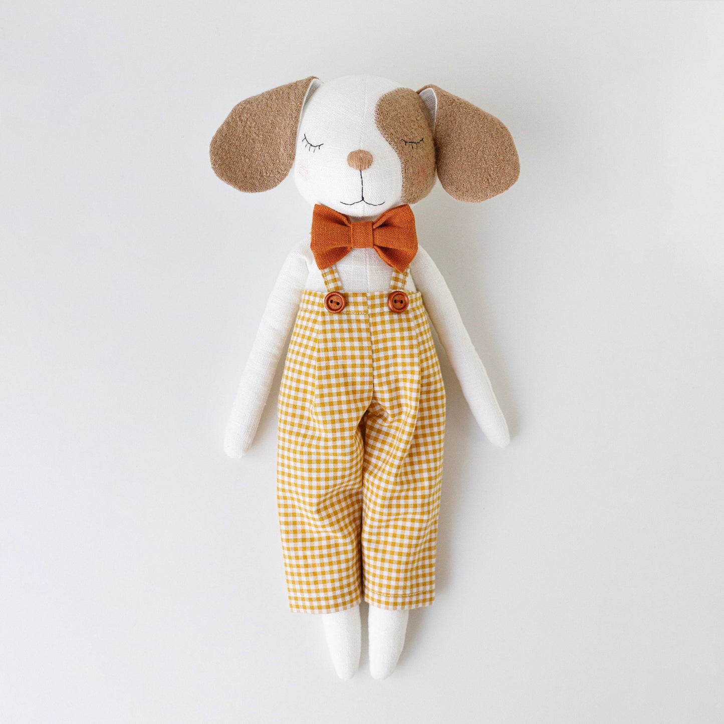 Stuffed dog toy with a bow tie and checkered pants on a white background