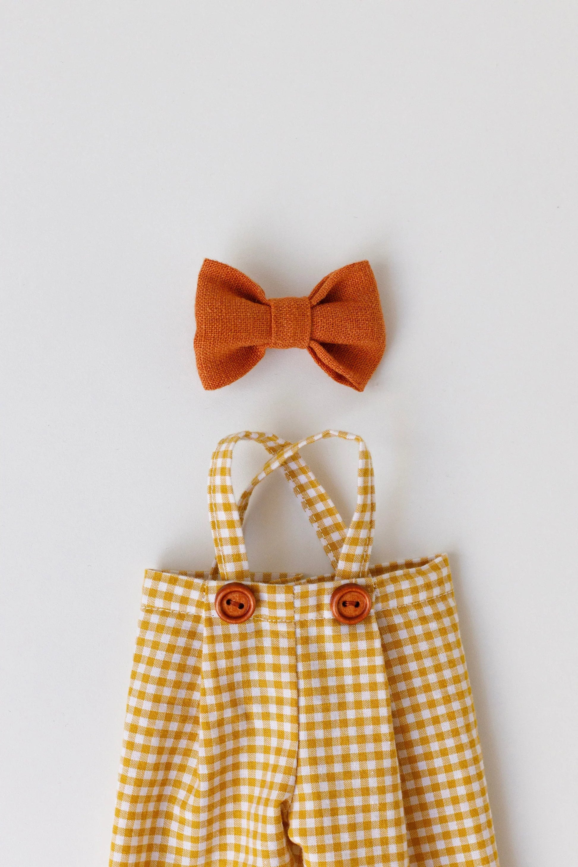 Yellow checkered romper with suspenders and orange bow tie on a light gray background