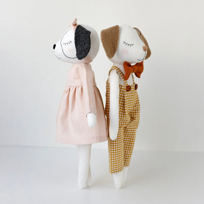 Two plush dog toys, one in a pink dress and the other in checkered overalls with a bow tie, on a white background.