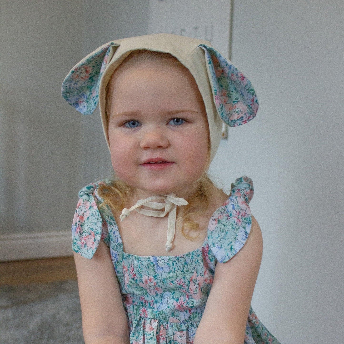 Child wearing a floral dress and bonnet with bunny ears against a neutral background