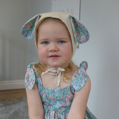 Child wearing a floral dress and bonnet with bunny ears against a neutral background