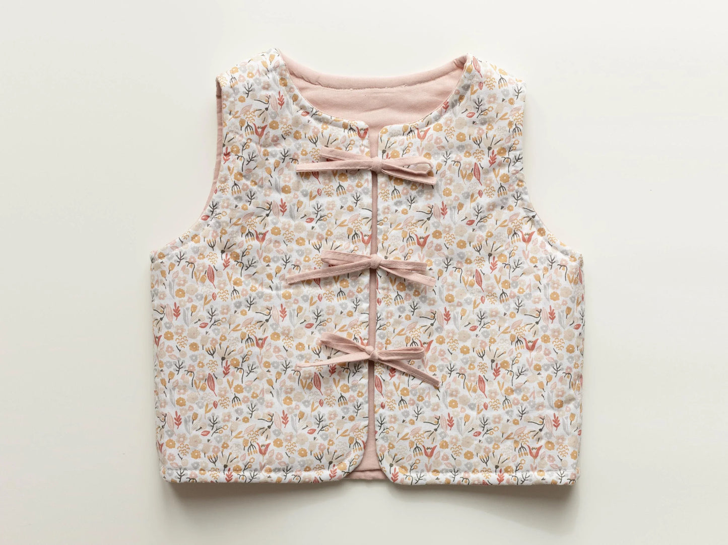 Floral-patterned children's vest with pink ribbons on a light background