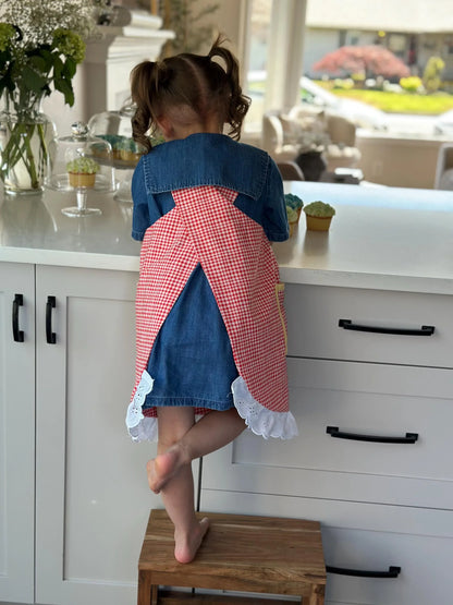 Child in a red and blue dress standing on a step stool in a kitchen.